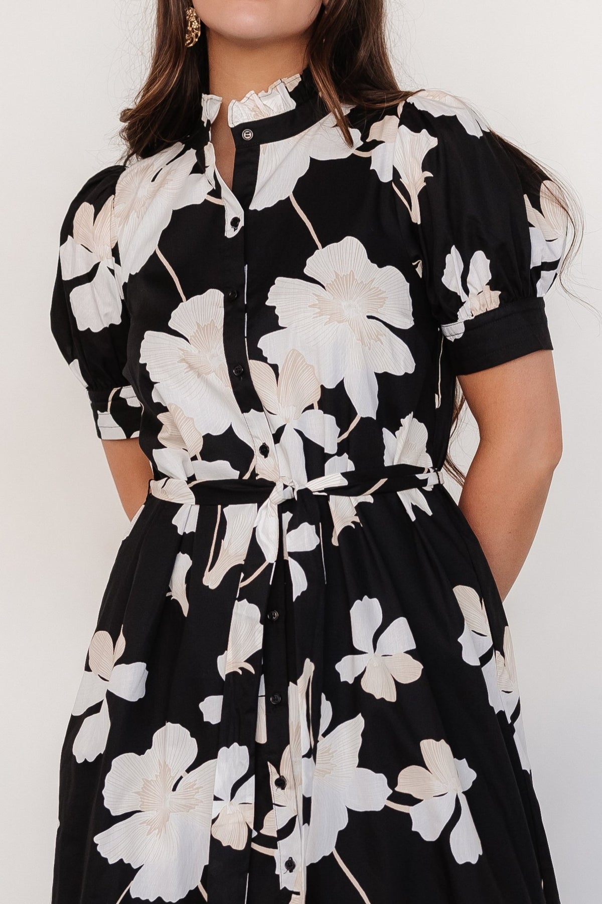 Close-up of dress bodice showing functional front buttons, ruffle-collared neckline, fitted short sleeve cuff, and floral print details.