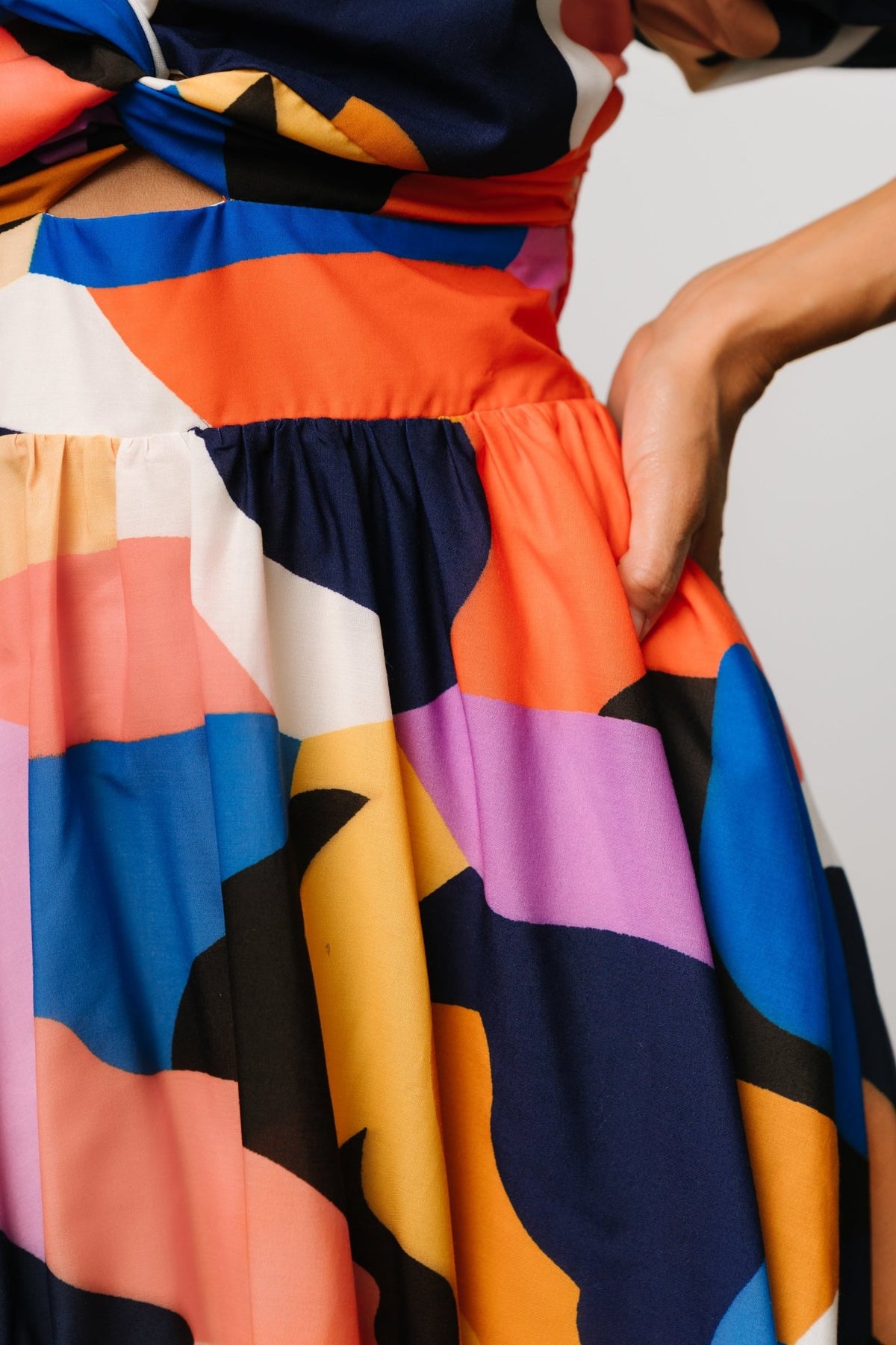 Model poses with hands in hidden pockets wearing rust and navy multi Lola midi dress, highlighting practical pocket placement.