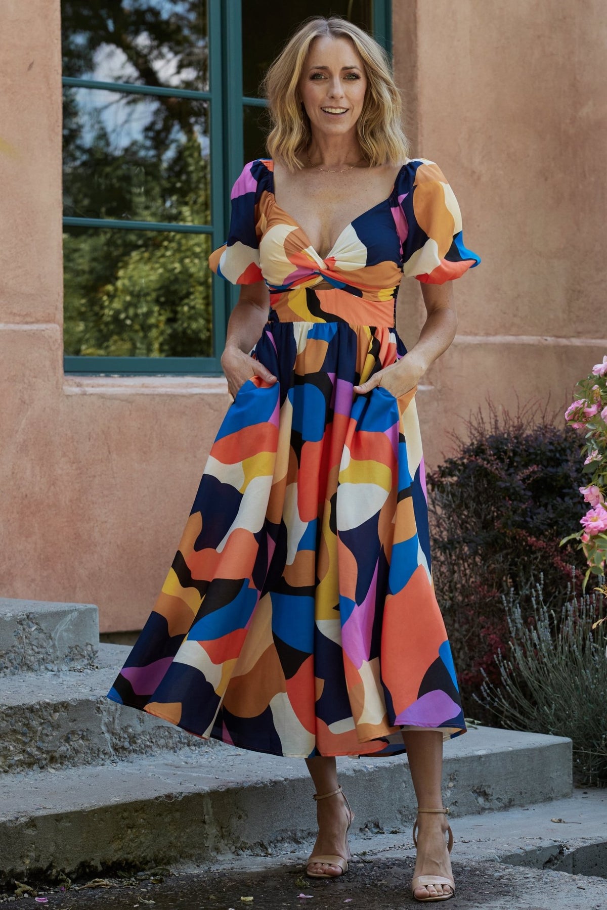 Model wearing Lola midi dress in rust and navy multi, three-quarter pose highlighting puffed sleeve and knee-length swing.