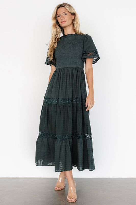 Dark green Loveland Geo Lace Maxi Dress on model, showing ruffled neckline, smocked bodice, oversized short sleeves, and tiered skirt with pockets.