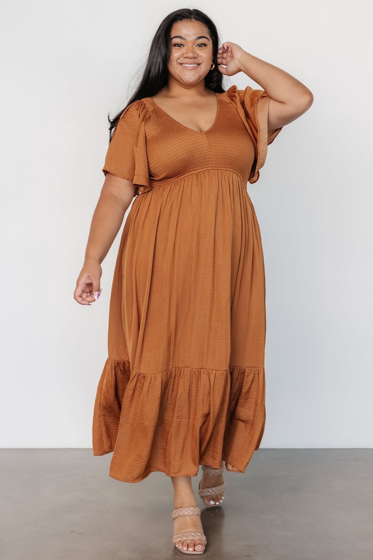 Full-length view of dark copper midi dress on model highlighting semi-pleated ruffle hem and flowy skirt movement.