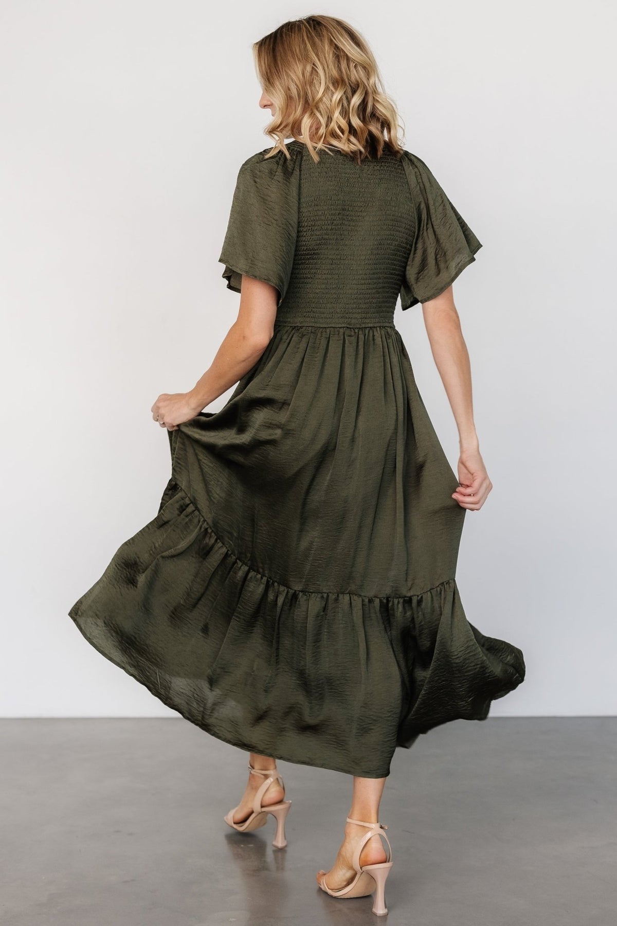 Back and side view of Lovell smocked midi dress in deep olive showing mid-length skirt and semi-pleated ruffle hem movement.