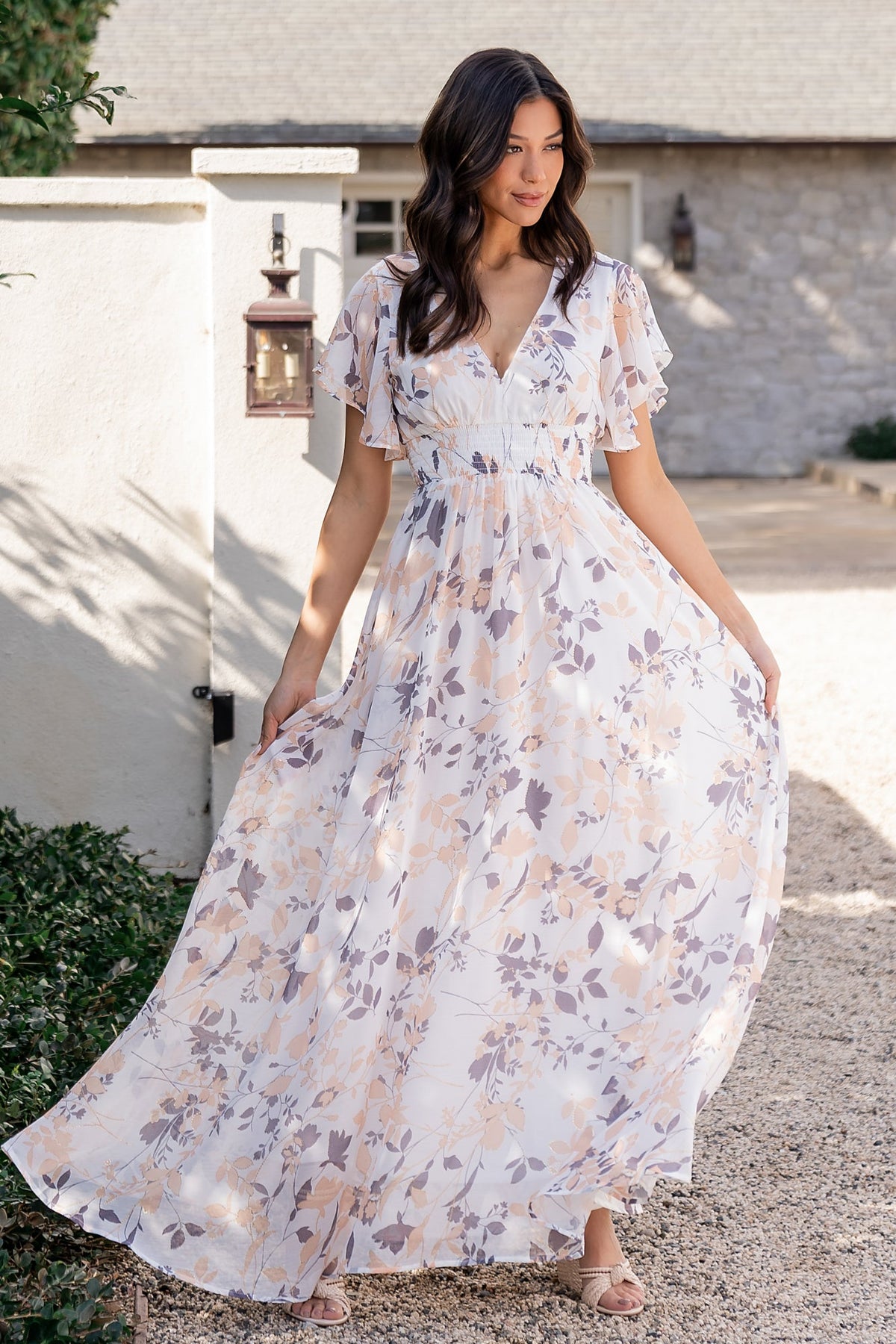 Close-up of off-white chiffon fabric showing metallic floral accents, delicate flutter sleeve, and V-neckline with smocked waist detail.