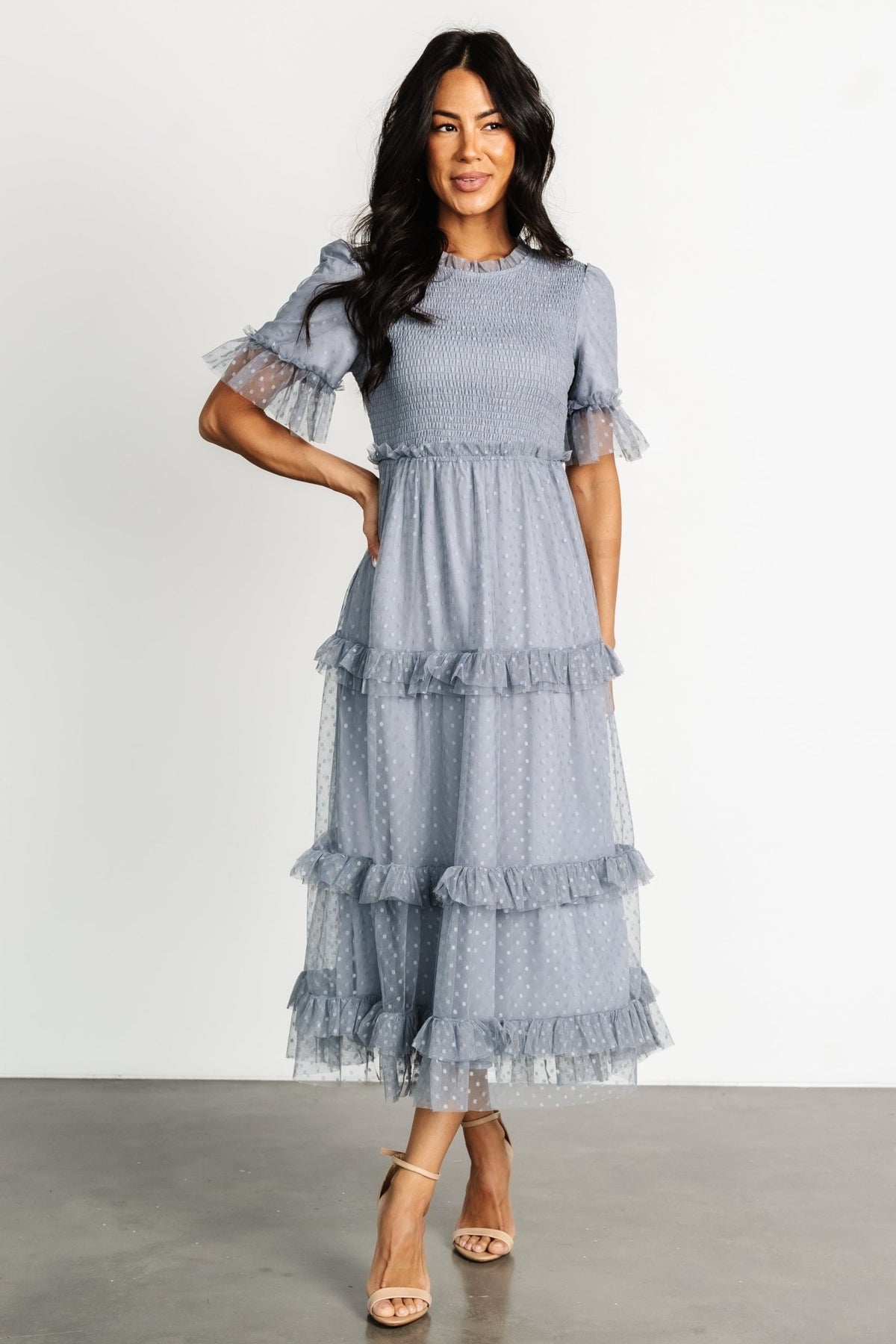 Front view of Lysandra smocked dot midi dress in dusty slate tulle showing ruffled high neckline, smocked bodice, and tiered ruffle skirt in soft light.