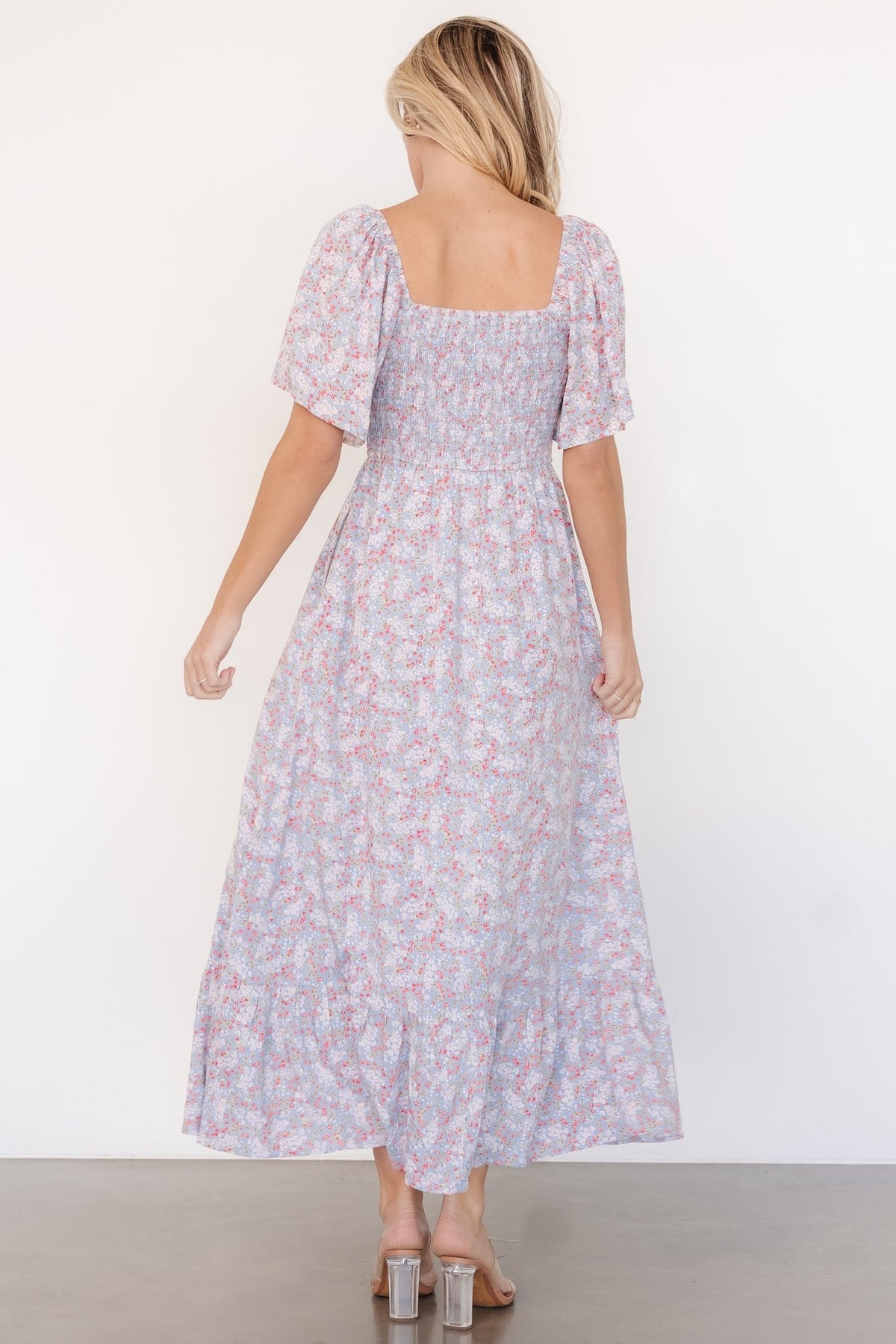 Detail of short flutter sleeve and floral fabric on Lyssa smocked midi dress in dusty blue with red, white, and pink floral motifs.