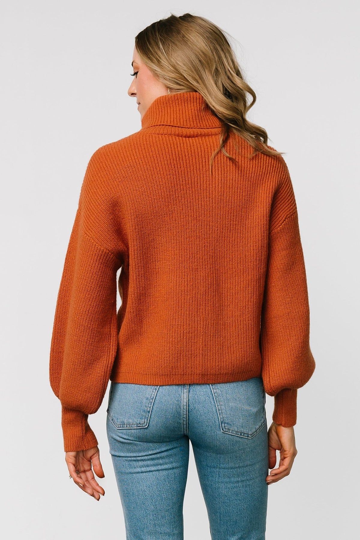 Detail shot of ribbed stitch pattern and knit density on spice turtleneck sweater, highlighting fabric texture and color.