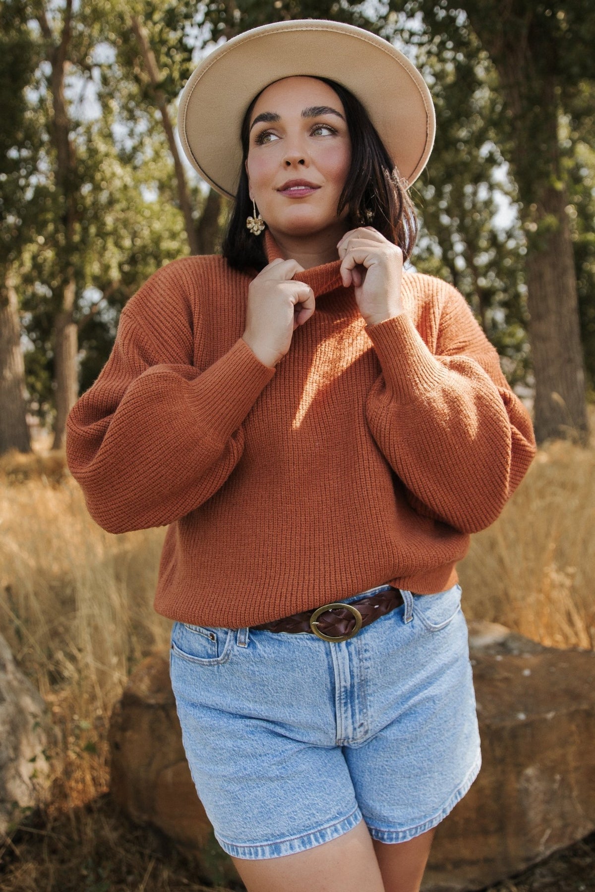 Model wearing spice ribbed turtleneck sweater styled with jeans; shows relaxed silhouette, long bubble sleeves, and high turtle neckline.