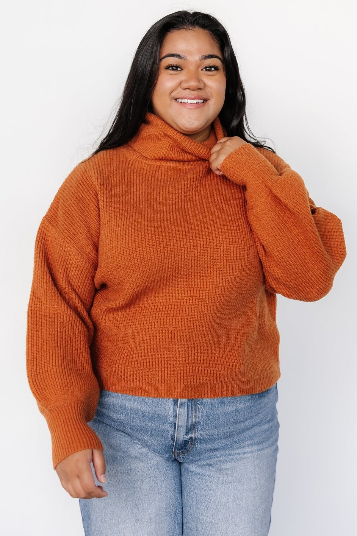 Close-up of ribbed knit texture and structured turtle neckline on a spice-colored sweater; shows stitch detail and soft finish.
