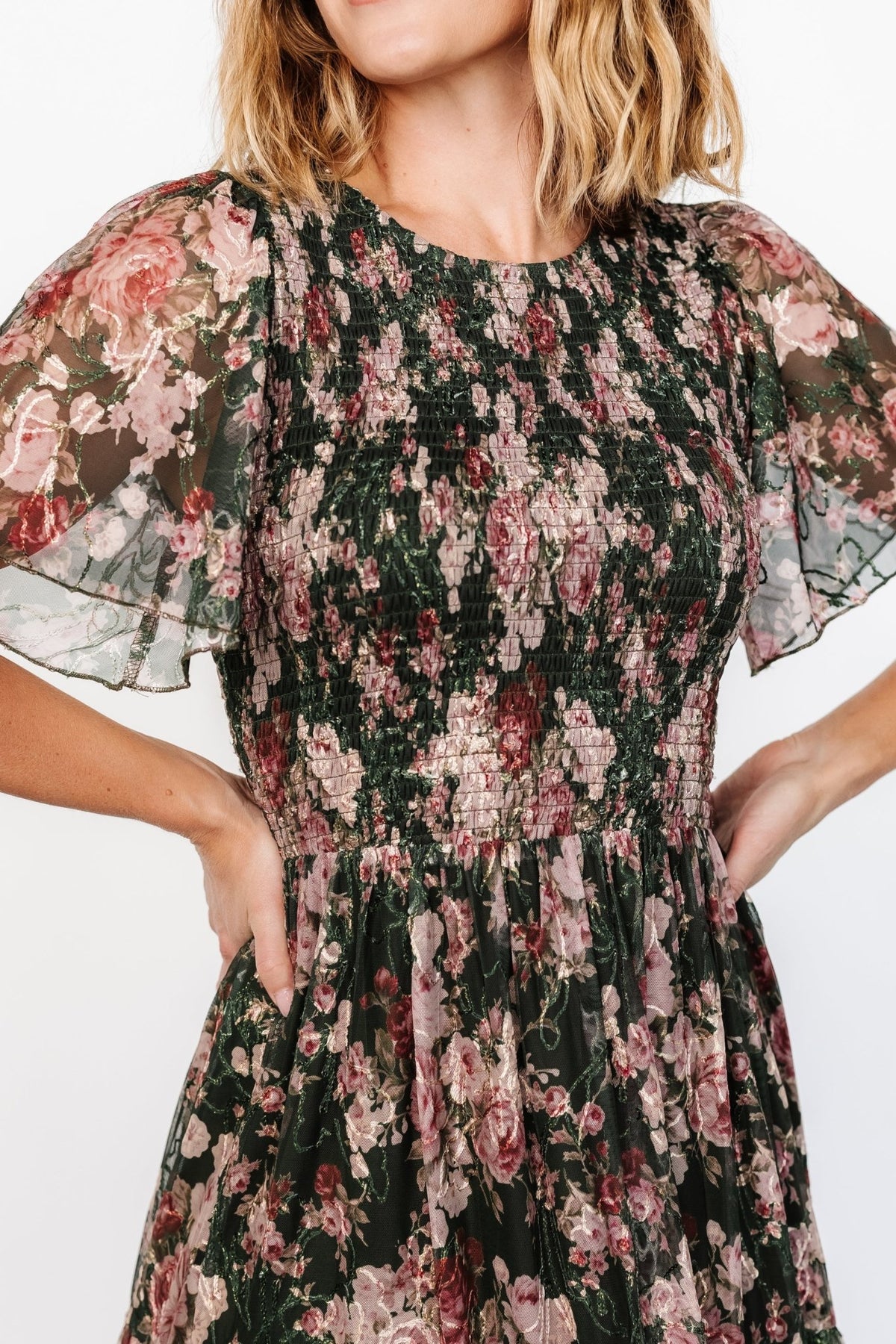 Close-up of embroidered floral tulle showing blush and berry threadwork with subtle gold metallic stitching and texture.