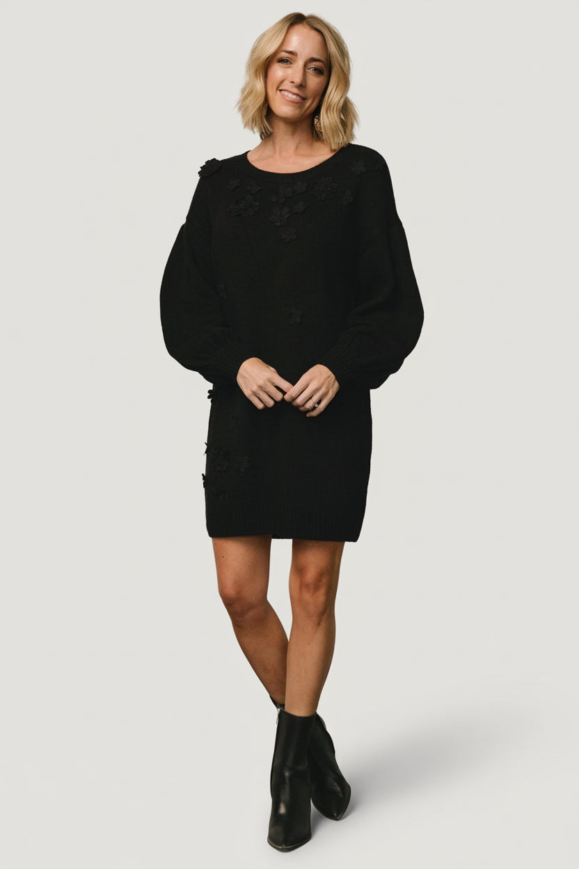 Front view of the Margaux sweater dress in black showing floral applique detail, round neckline, dropped shoulder and ribbed hemline, on model.