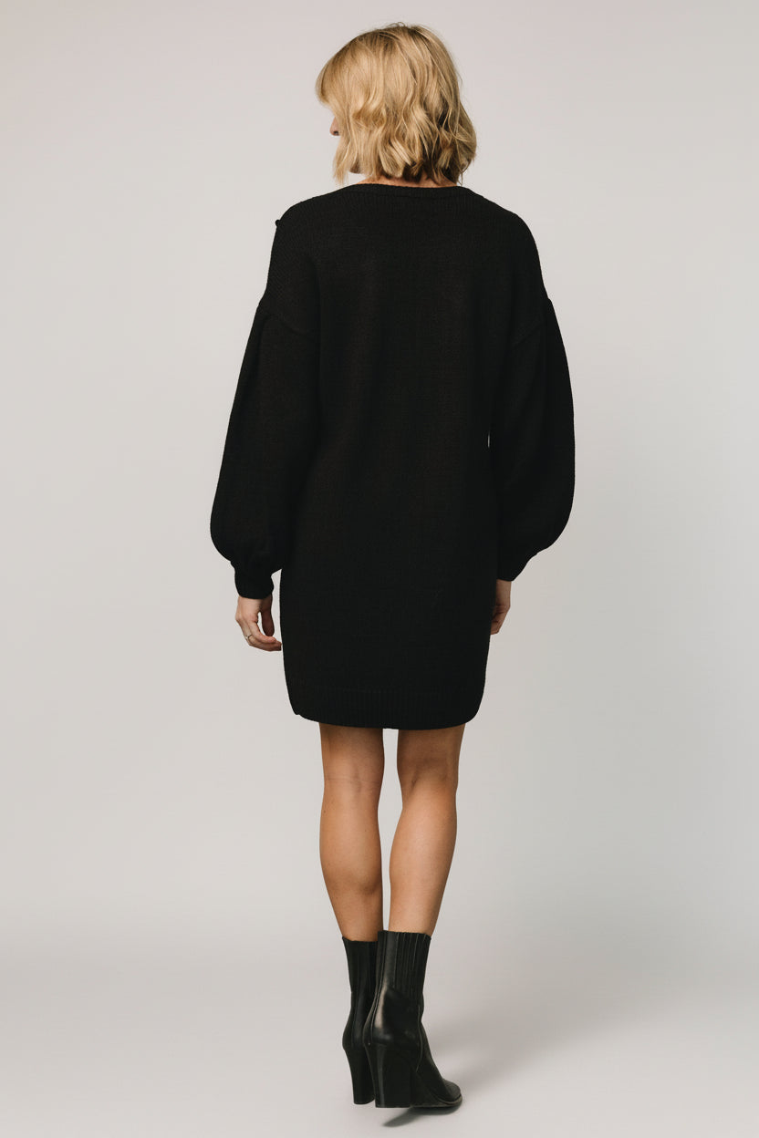 Full-length image of Margaux black sweater dress styled with boots to show length, dropped shoulder, and overall casual tailored appearance on model.