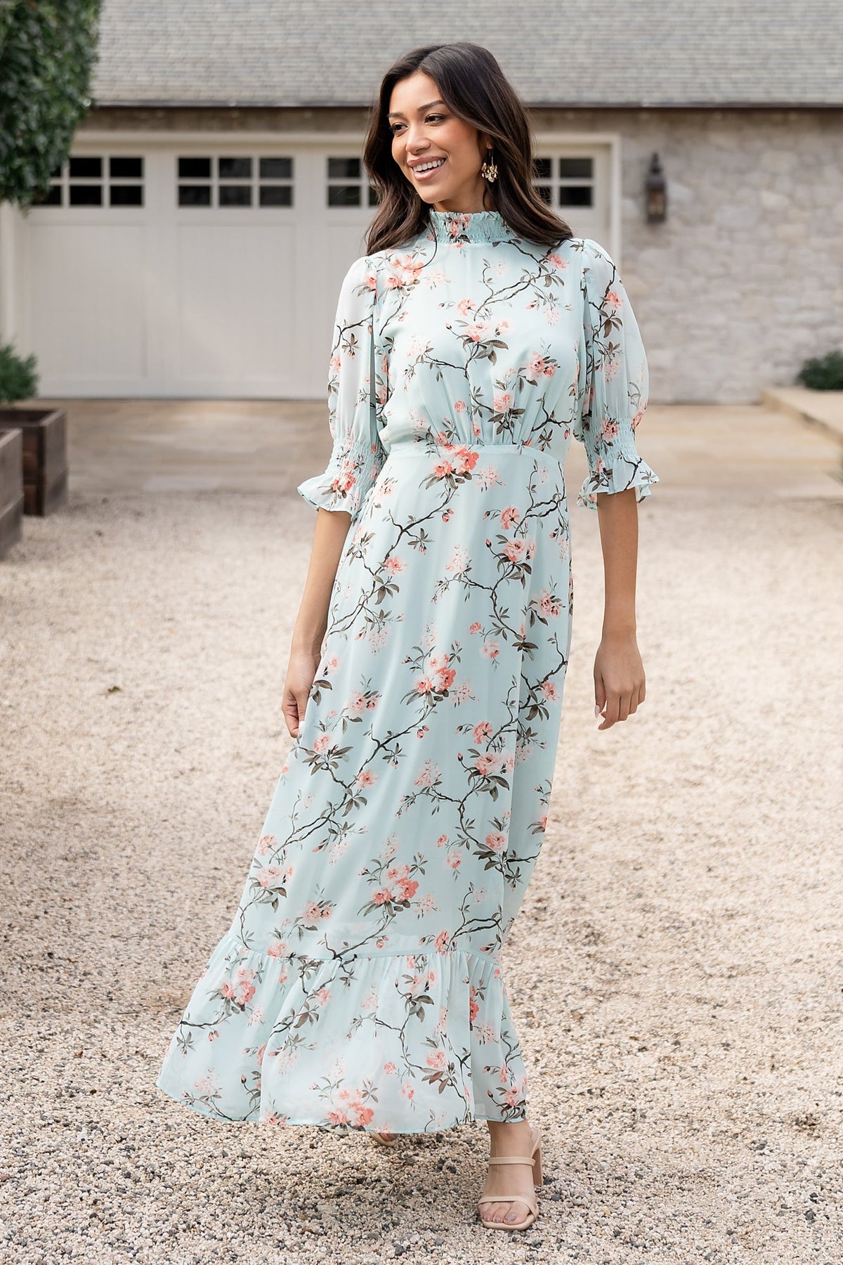 Model wearing Marie Mock Neck Maxi Dress in sage floral, showing smocked ruffle sleeves, pleated front waist and flowing chiffon skirt.