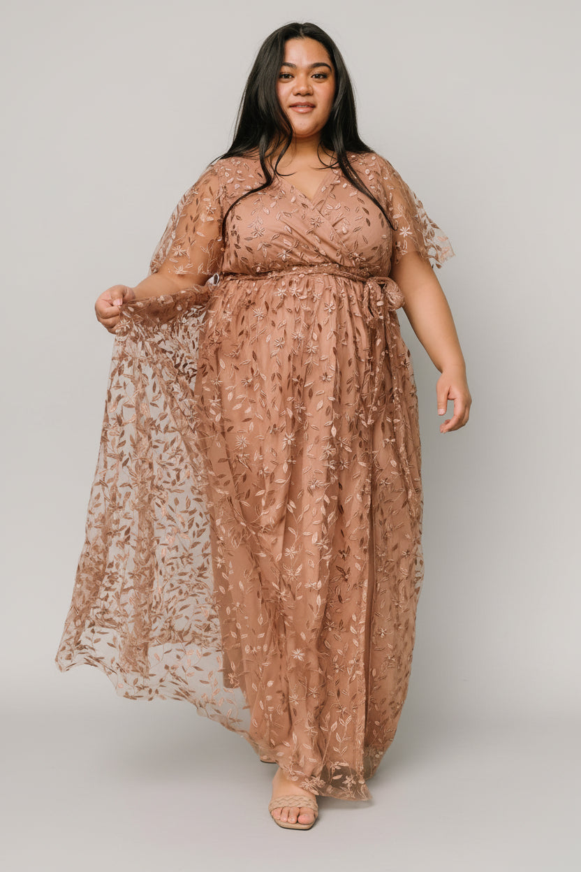 Three-quarter side view showing short unlined sleeves and left-leg slit on a nude-rose embossed organza maxi dress.
