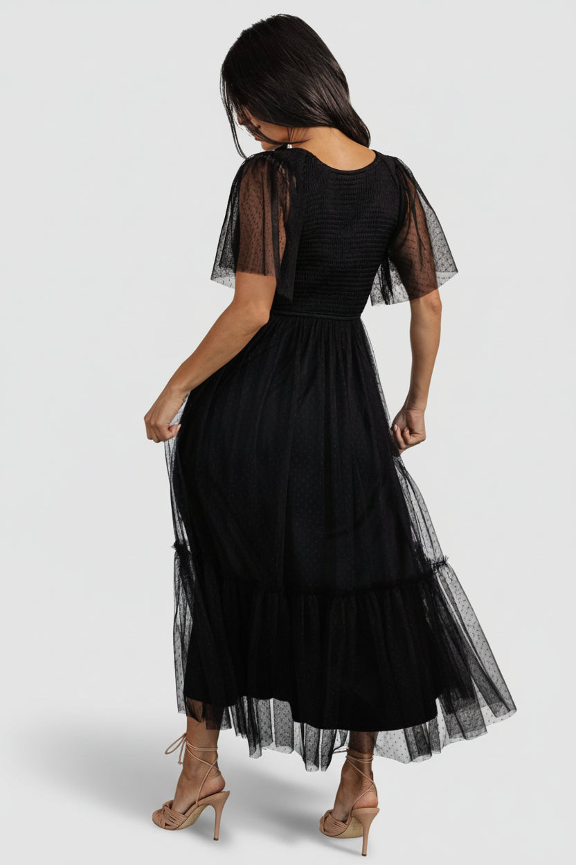 Full-length image of black smocked tulle midi dress styled for occasion wear, suitable for wedding guest, bridesmaid or cocktail events.
