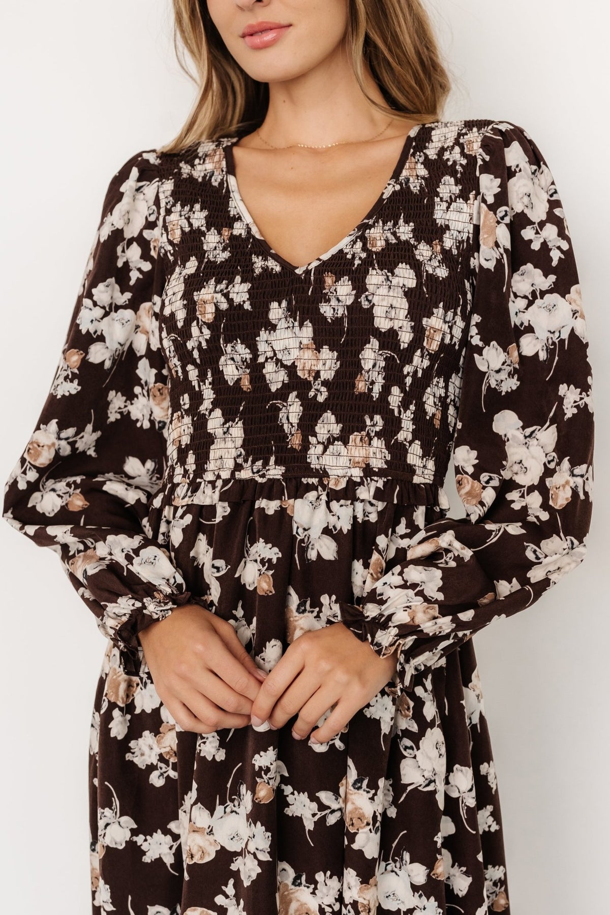Close-up of smocked bodice showing elastic smocking, V-neckline, and small neutral floral print on woven polyester fabric.