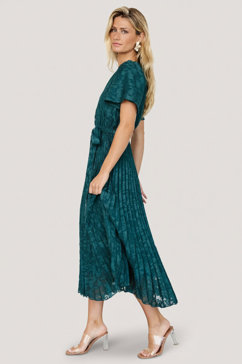 Styled outfit shot of emerald chiffon pleated dress paired with heels, showing silhouette, sash placement, and occasion styling ideas.