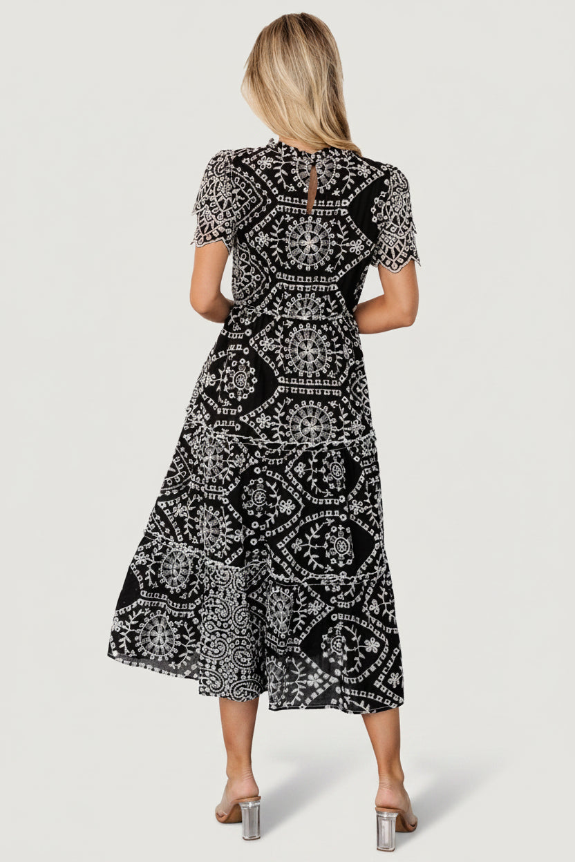 Studio shot of Mirabel midi dress on mannequin, displaying layered scalloped sleeves, high ruffled neckline and full embroidered pattern.