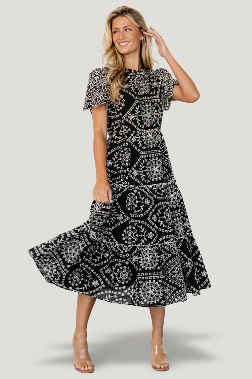 Front view of Mirabel embroidered eyelet midi dress in black with white floral embroidery, ruffled high neckline and scalloped short sleeves.