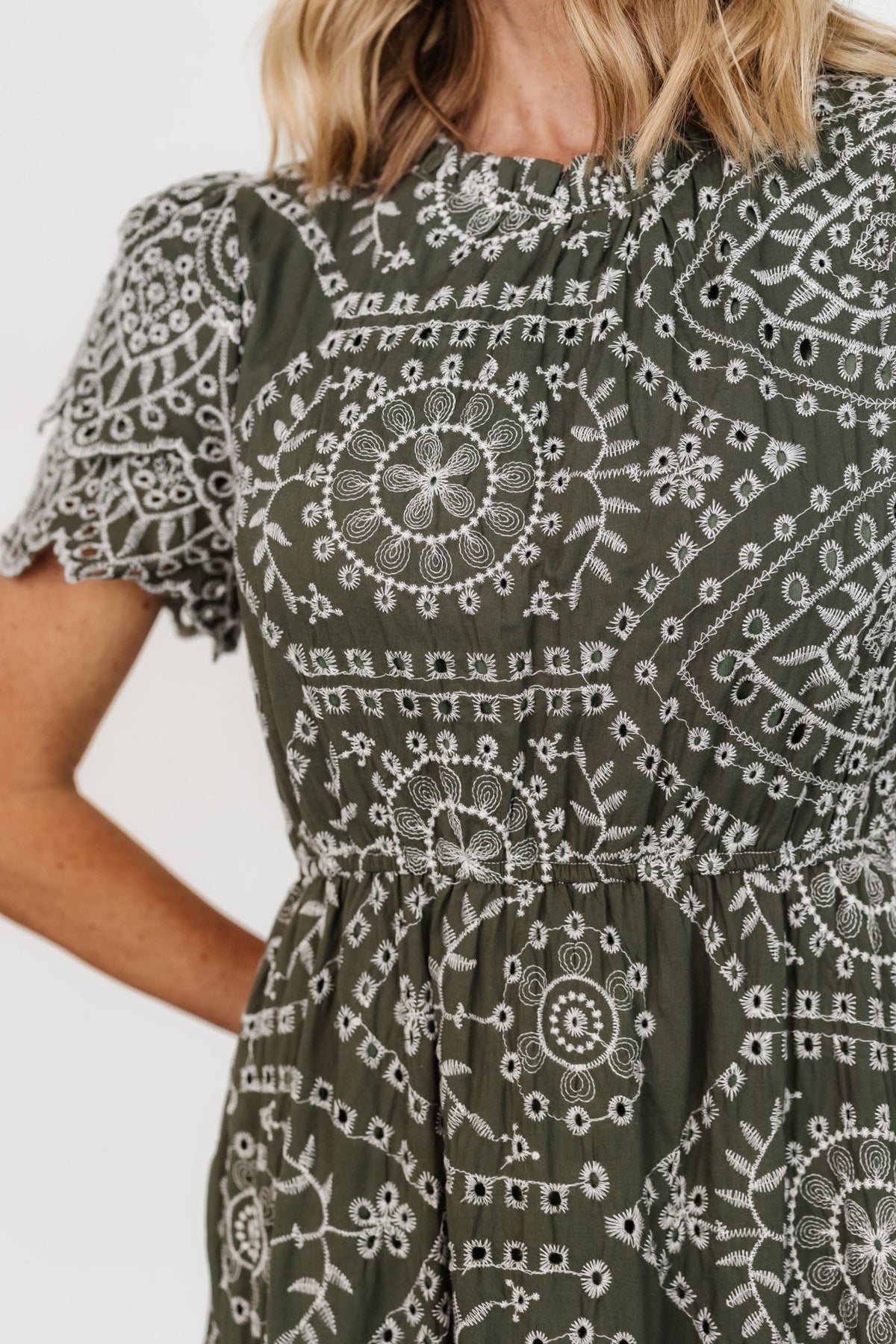 Back view showing keyhole-and-button closure, elasticated waist, and tiered skirt on the Mirabel Eyelet Midi Dress in olive and white.