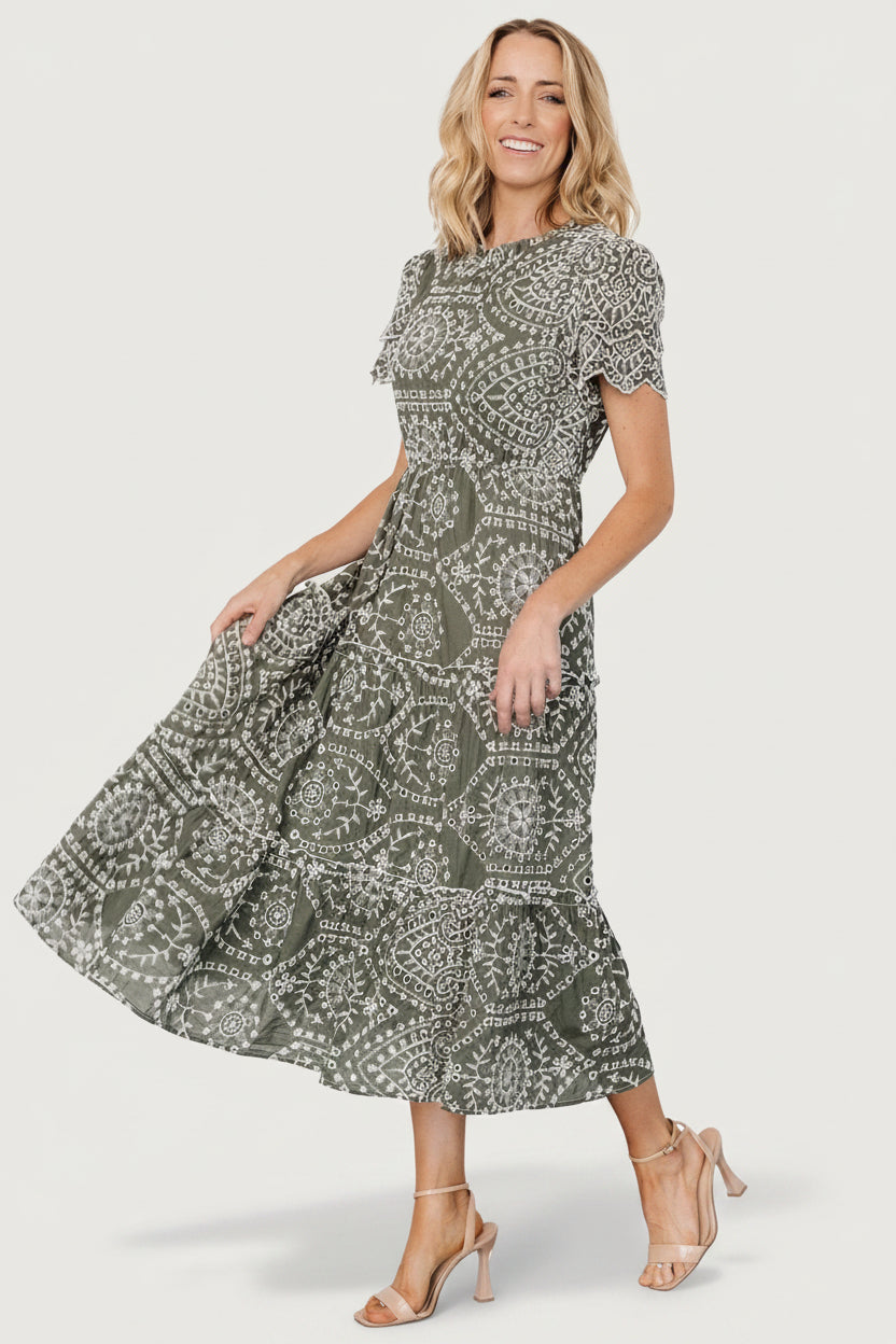 Studio shot highlighting tiered midi skirt, ruffle trims, and movement of the Mirabel Eyelet Midi Dress in olive and white.