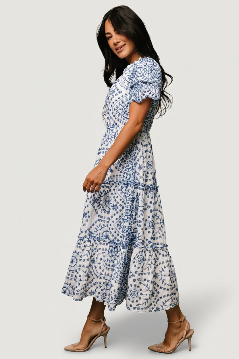 Detail image of the tiered midi skirt with soft ruffle tiers and scalloped hems on the white dress with blue embroidery.