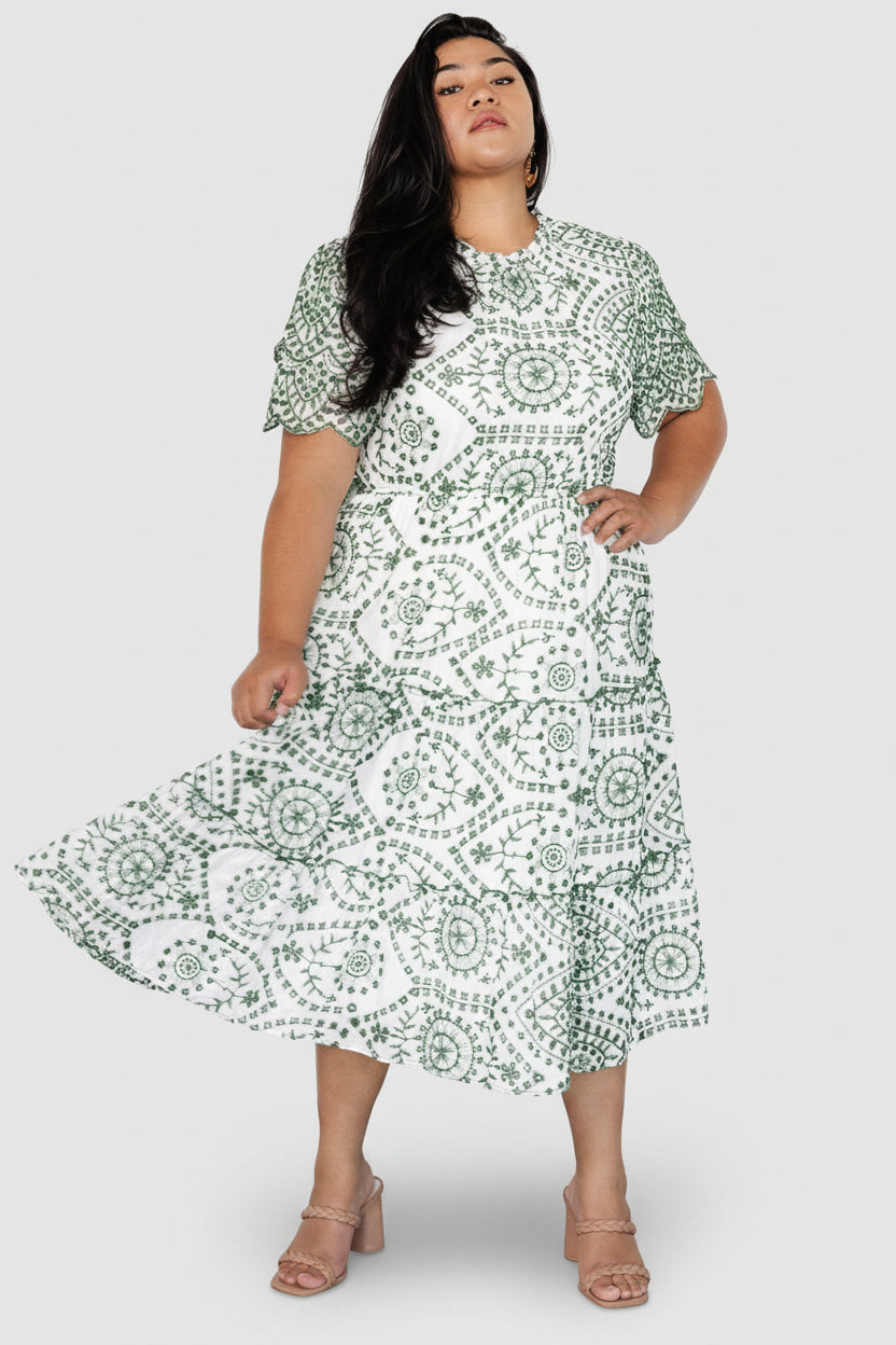 Model wearing Mirabel eyelet midi dress in white with Kelly green embroidery, showing short layered scalloped sleeves and elastic waist.