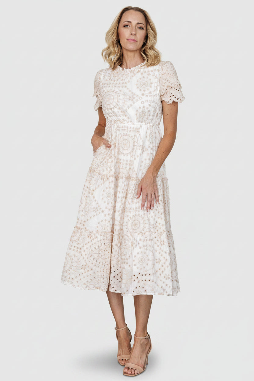 Front view of white midi dress with natural beige embroidered eyelet, high ruffled neckline, elastic waist and tiered skirt with ruffle trims.
