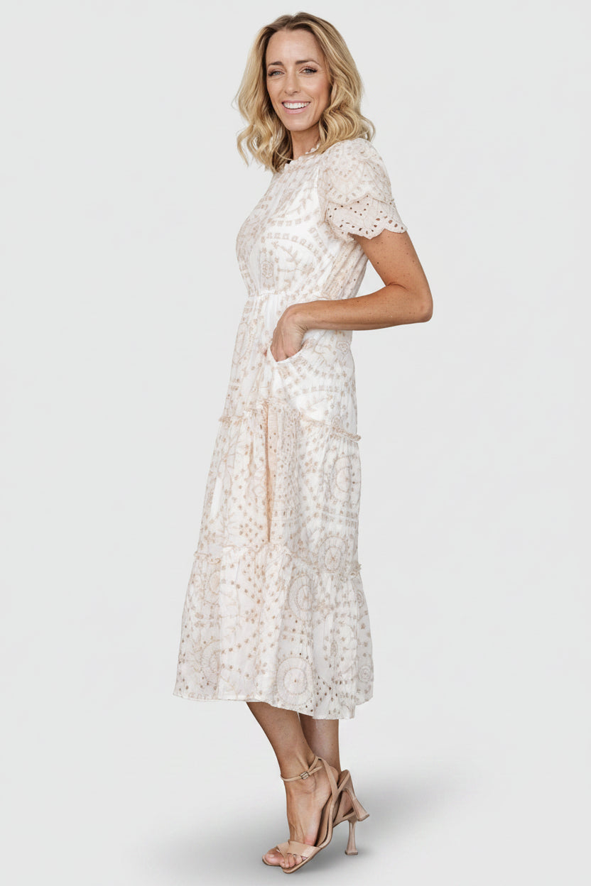 Styled flat-lay showing the full dress silhouette, embroidered eyelet pattern, scalloped sleeve detail, and tiered ruffle hemline.
