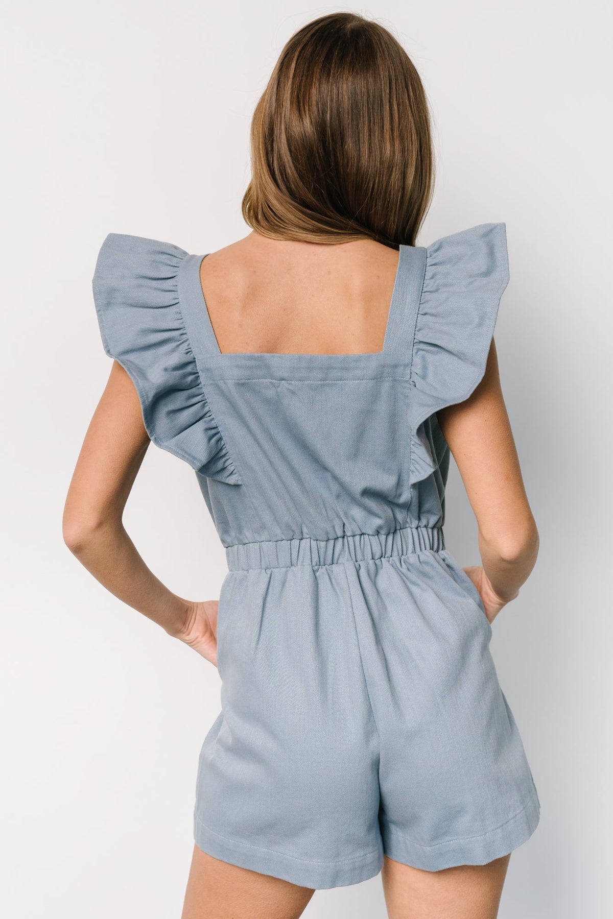 Close-up of the romper's center front zipper, square neckline edge, and denim-like weave showing the washed dusty blue finish and stitching details.
