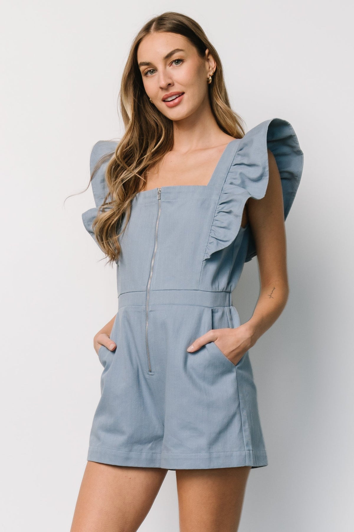 Back view of Montgomery Denim Romper showing elasticized back waist, short flutter sleeves, and the shorts hem in a soft dusty blue cotton-blend.