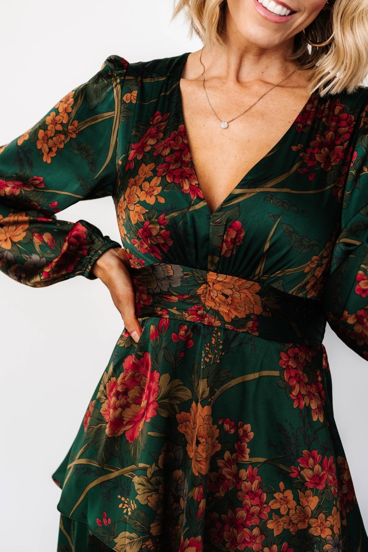 Three-quarter view of emerald floral satin maxi dress highlighting side silhouette, soft drape, and the dress’s flowing tiered ruffles in motion.