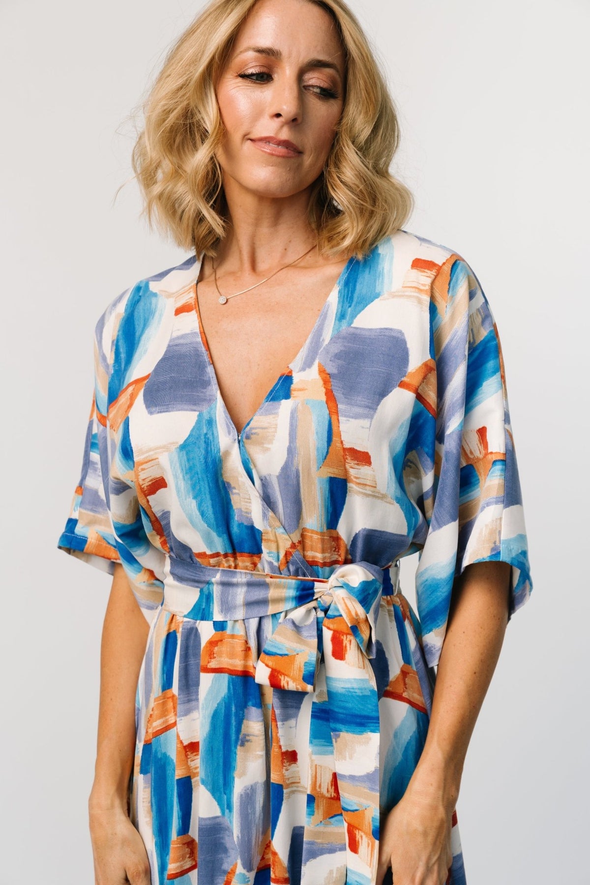 Model wearing blue and cobalt brushstroke-print maxi showing surplice V-neckline with hidden snap and elastic high waist detail.
