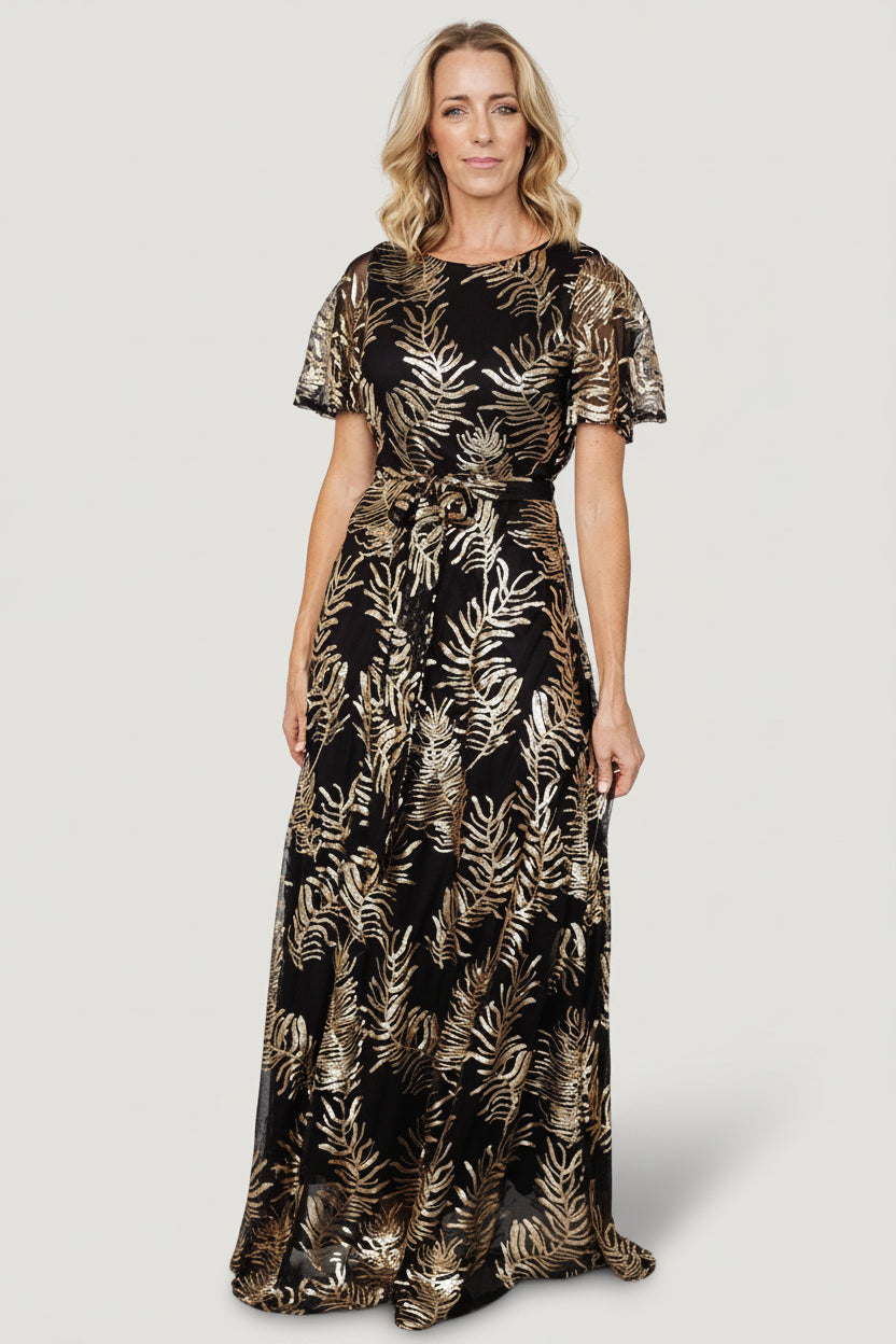 Front view of black sequin maxi dress with gold leaf sequin detail, round neckline, short sheer sleeves, waist sash.