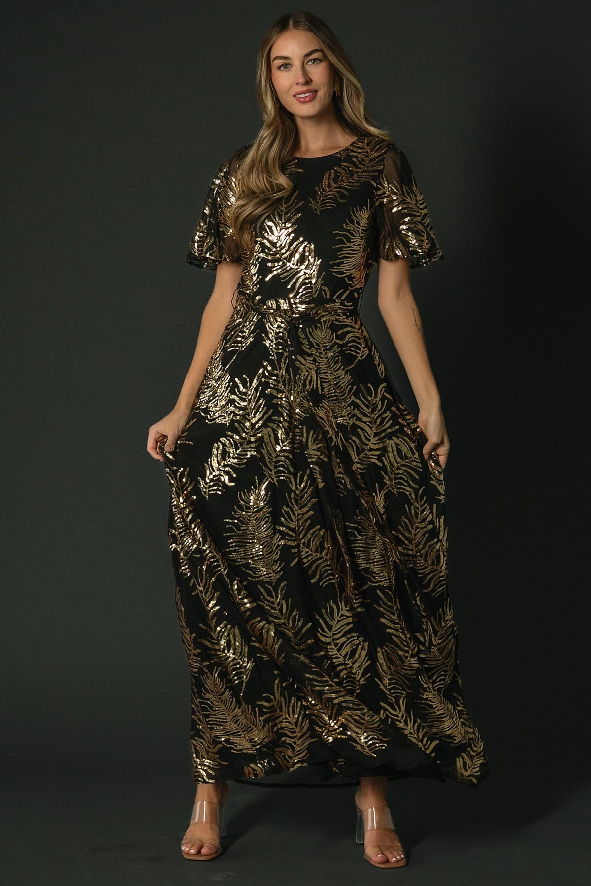 Studio image of full-length black and gold sequin gown styled with minimal jewelry and heels, ideal for weddings and formal events.