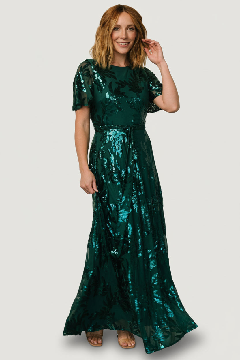 Front view of Muse Sequin Maxi Dress in emerald green on model, showcasing monochromatic sequin leaf detail, waist sash, and full-length skirt.