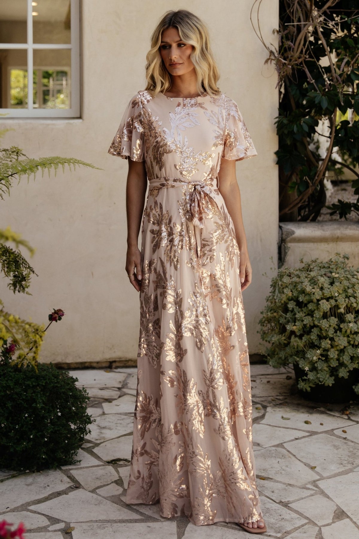 Model walking in the rose-gold sequin maxi dress to show skirt movement and how the sequins catch light during motion for a subtle sparkle.