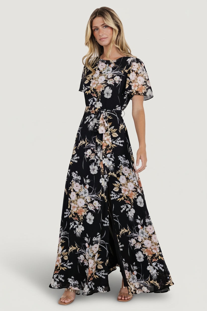 Front model view of black floral chiffon maxi dress with jewel neckline, short flutter sleeves, and removable belt.