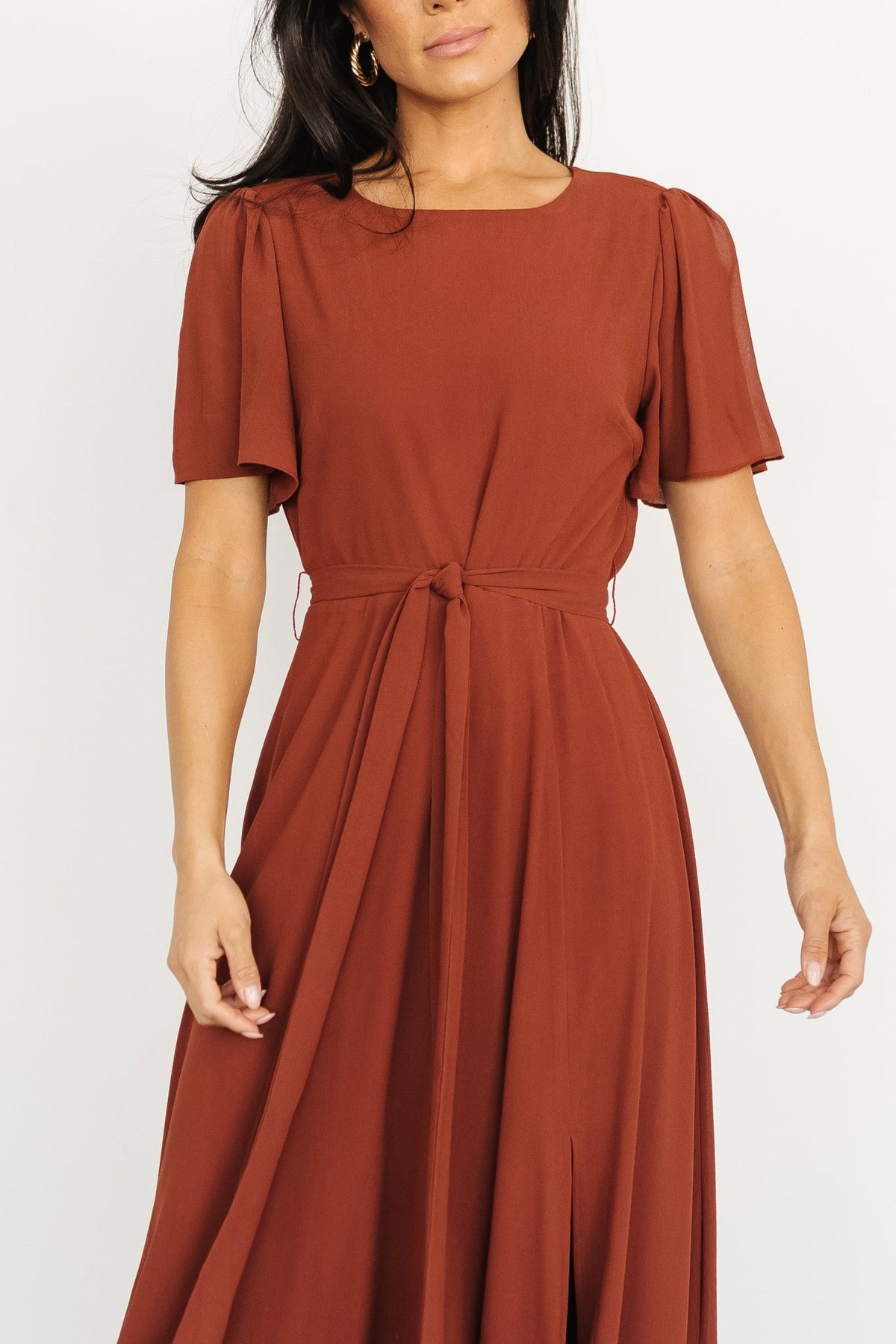 Three-quarter view of Naomi cinnamon chiffon maxi dress demonstrating the removable belt tie and maxi-length sweep.
