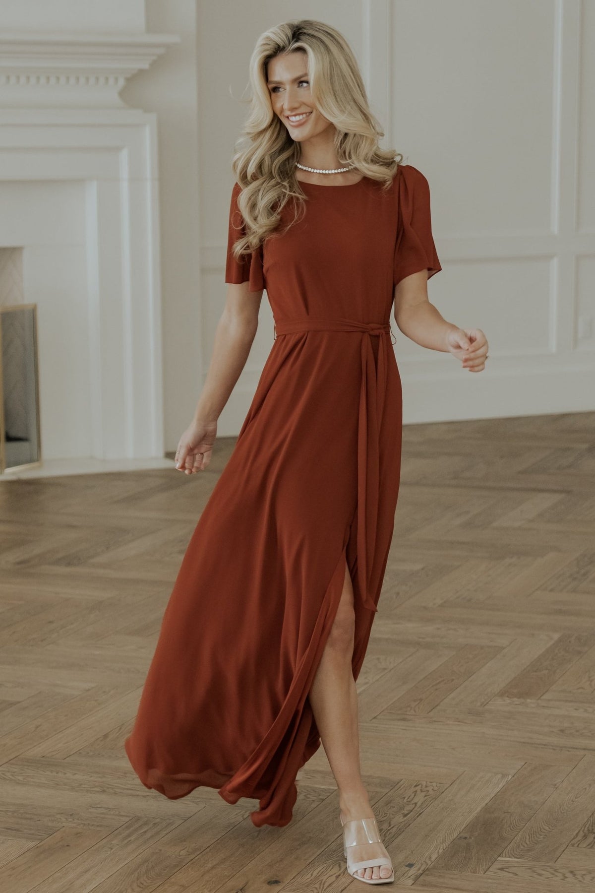 Side view of Naomi cinnamon chiffon maxi dress highlighting the left leg slit and natural waist tie in soft lighting.