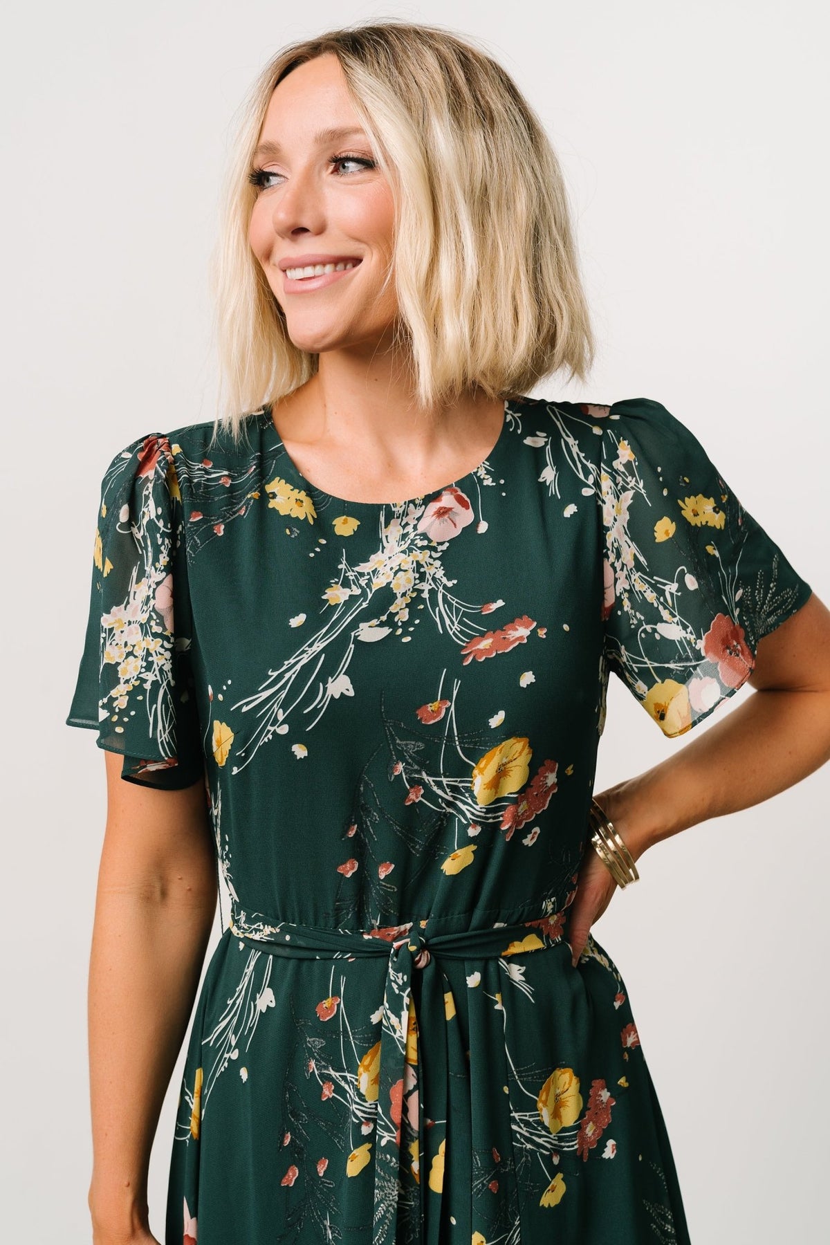 Close-up of short flutter sleeve and fabric detail on the dark green floral chiffon maxi dress, showing print and texture.