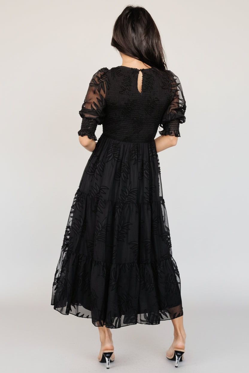 Styled editorial shot of the Nellie smocked midi dress in black showing full skirt tiers, fitted smocked bodice, and graceful movement of the fabric.