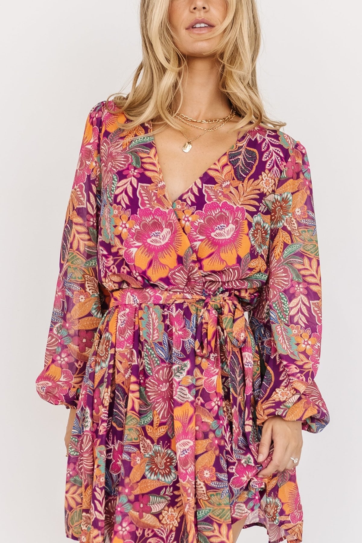 Three-quarter shot showing surplice V-neck and elastic gathered cuffs on the Newark mini dress in purple multi floral print on a standing model.