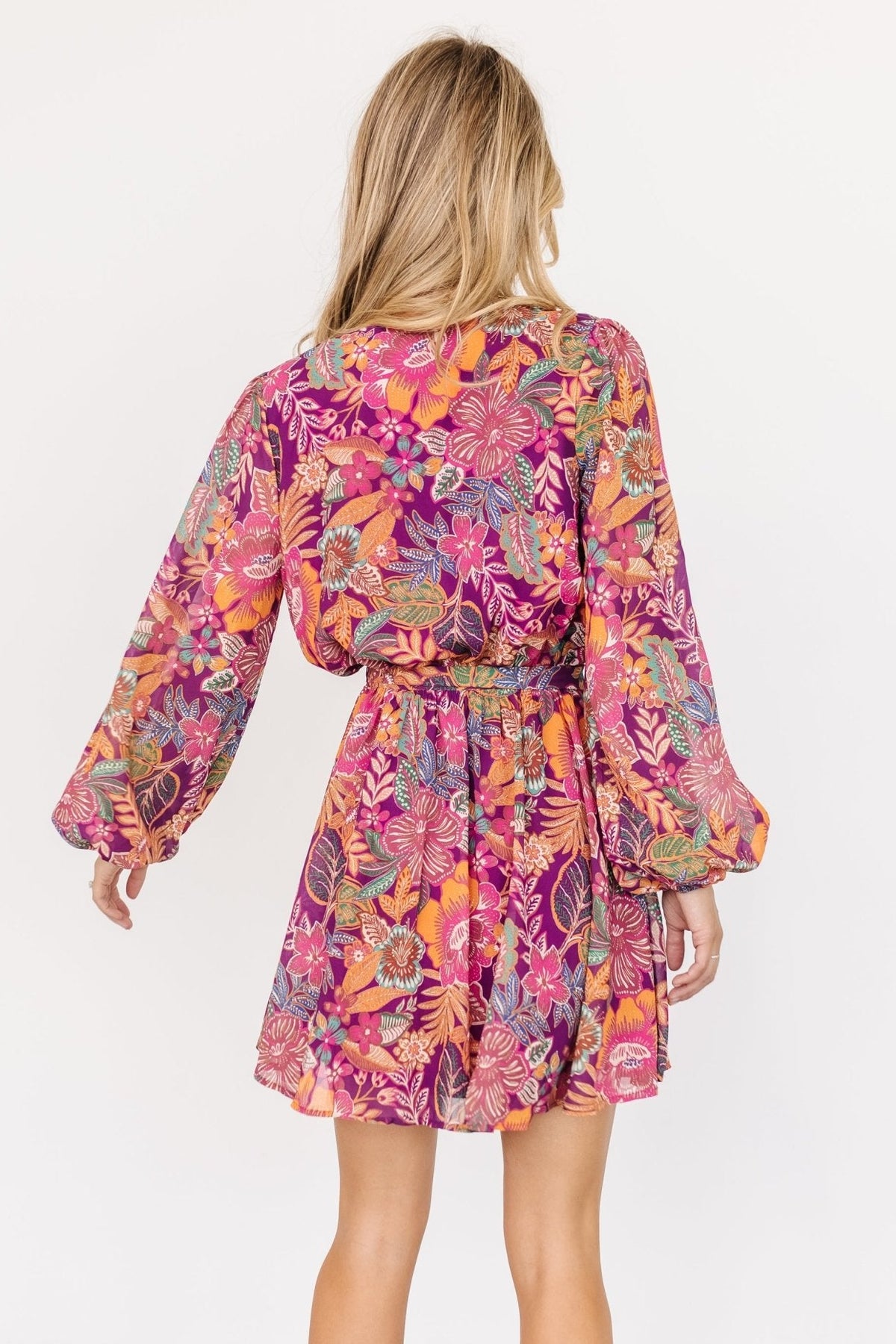 Styled outfit shot of Newark faux-wrap mini dress paired with neutral sandals; highlights removable waist tie and playful purple multi print.