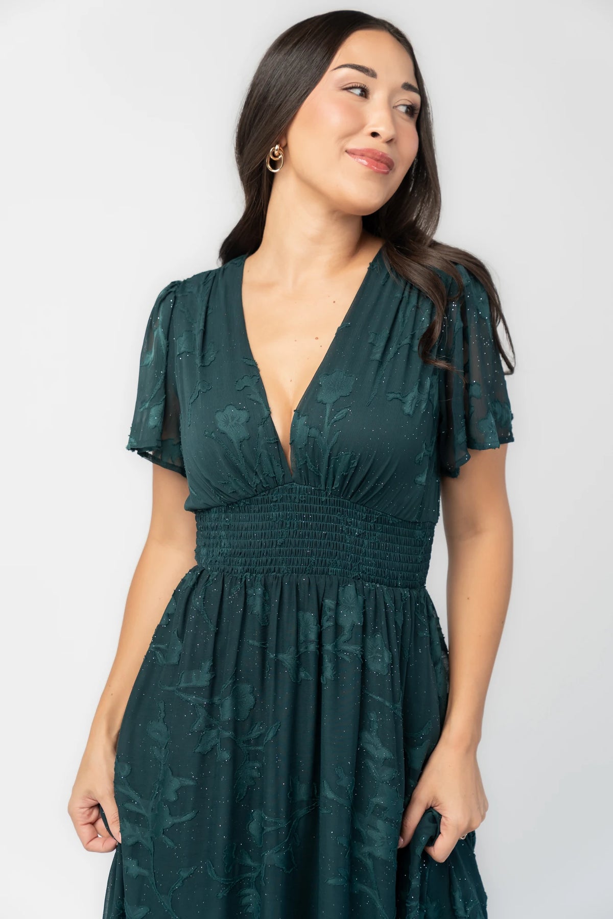 Noelle Maxi Dress in Dark Green Floral with silver sparkle, deep V-neck, flutter sleeves, smocked waist, and flowy skirt.