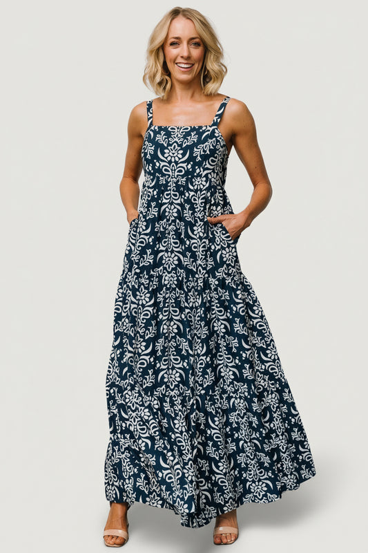 Front view of navy maxi dress with off-white print, square neckline, adjustable tank straps, paneled bodice and flowing tiered skirt for warm-weather wear.