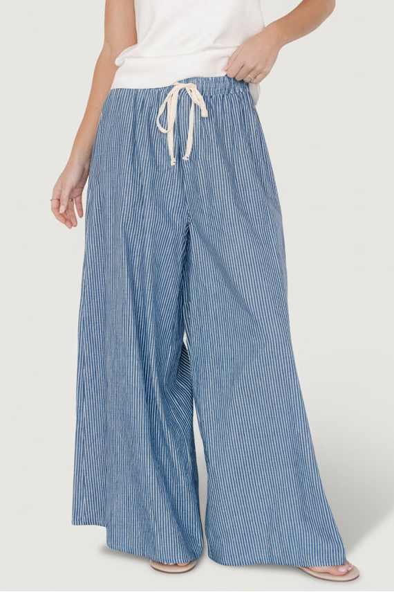 Front view of Odelia striped palazzo pants in blue with off-white vertical stripes, elastic waist and flowing wide-leg silhouette on a model.