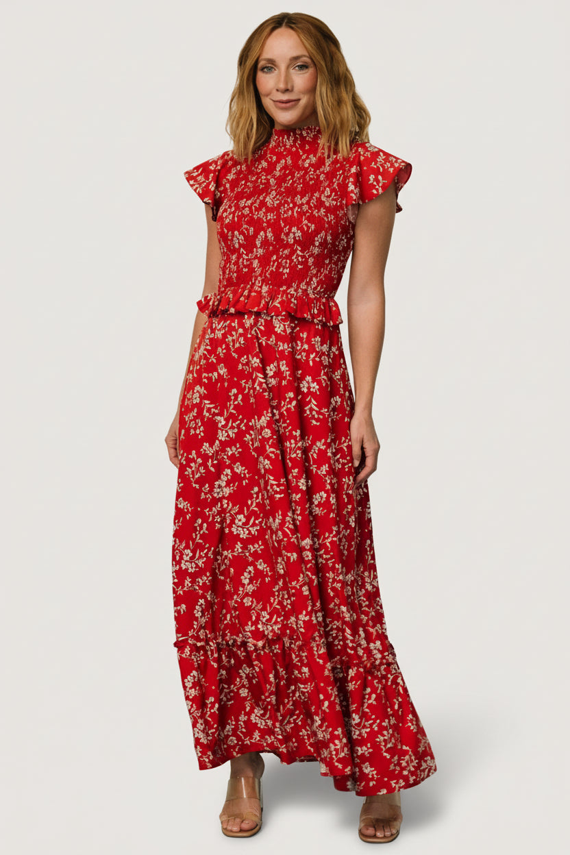 Front view of red floral chiffon maxi dress with smocked high neckline, smocked bodice and ruffle at natural waist, model standing.