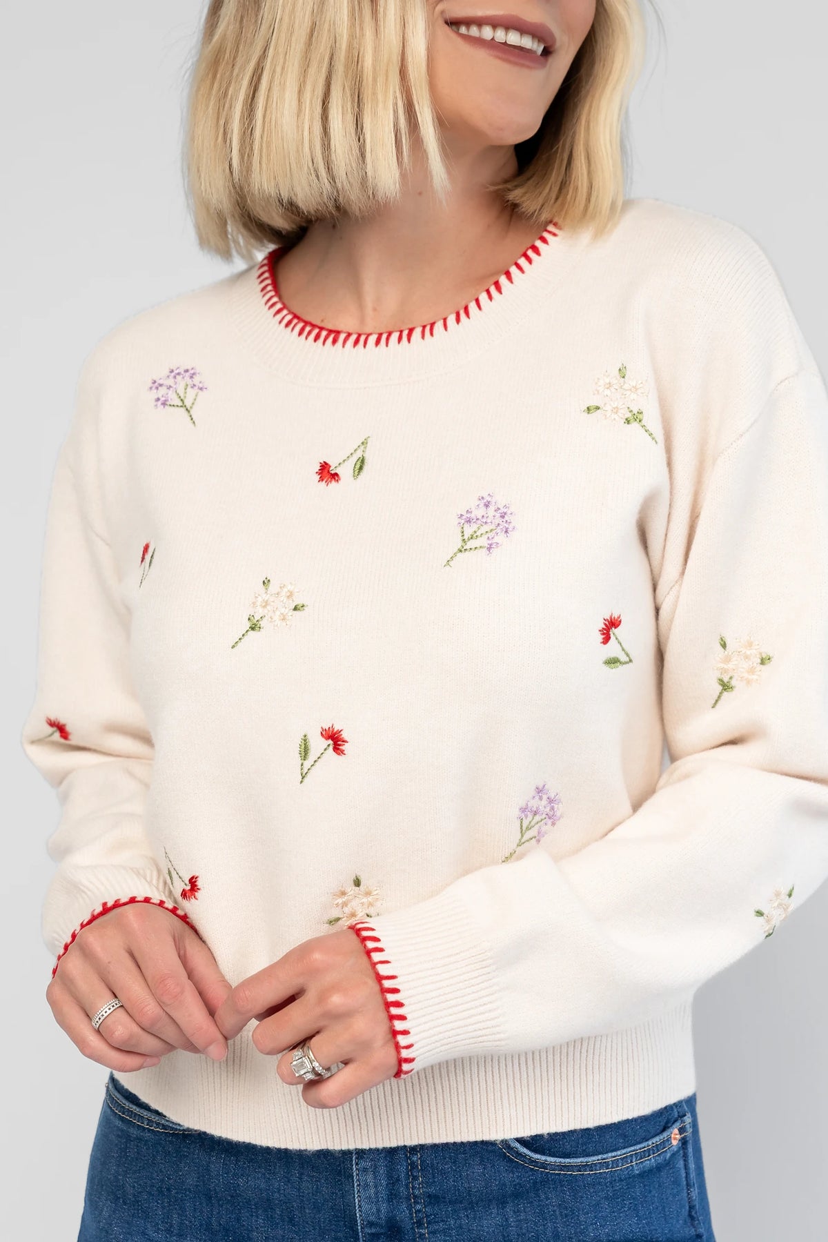 Ottilie Sweater in Cream with embroidered floral details, round neckline, red knit piping, and long sleeves.