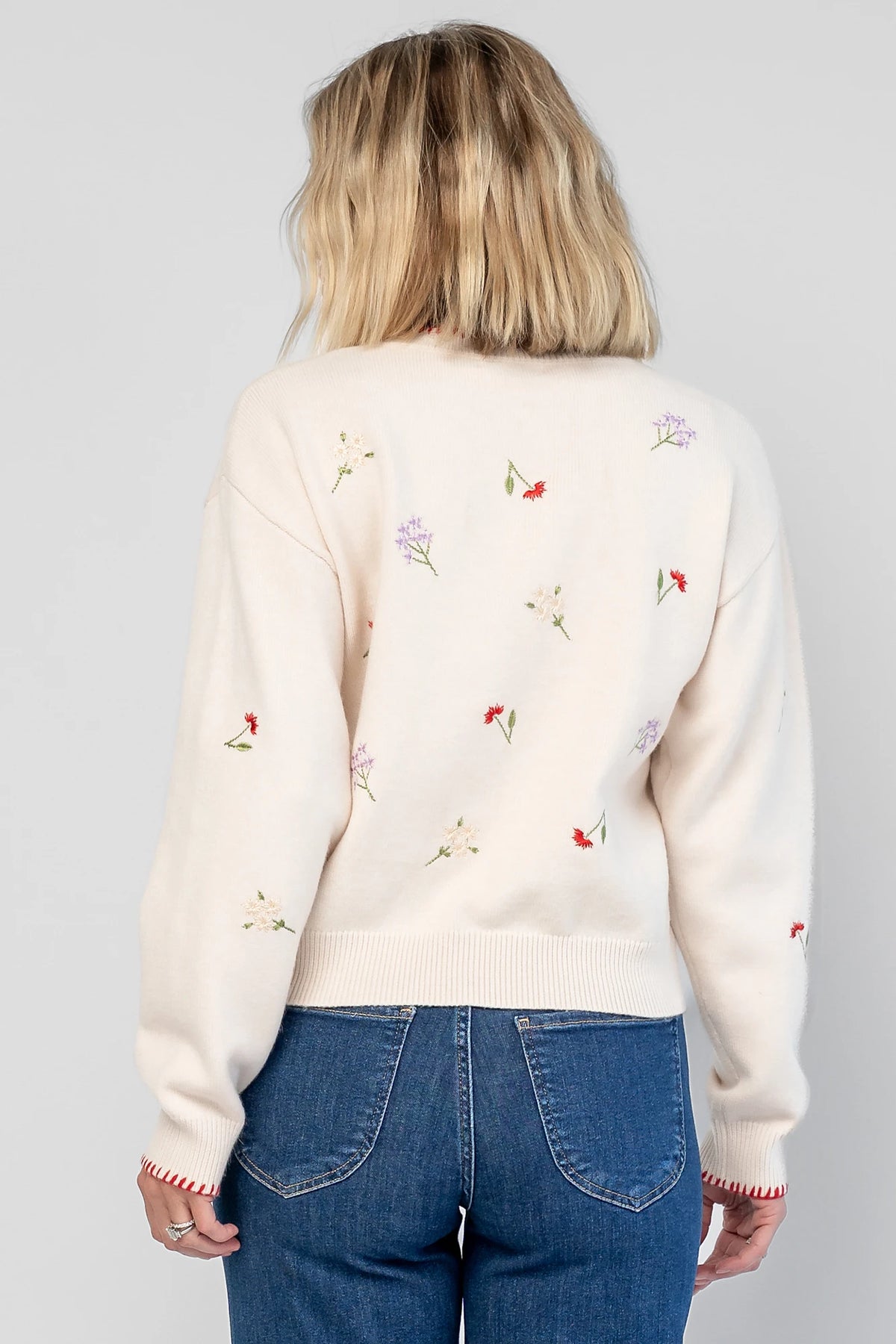 Ottilie Sweater in Cream with embroidered floral details, round neckline, red knit piping, and long sleeves.