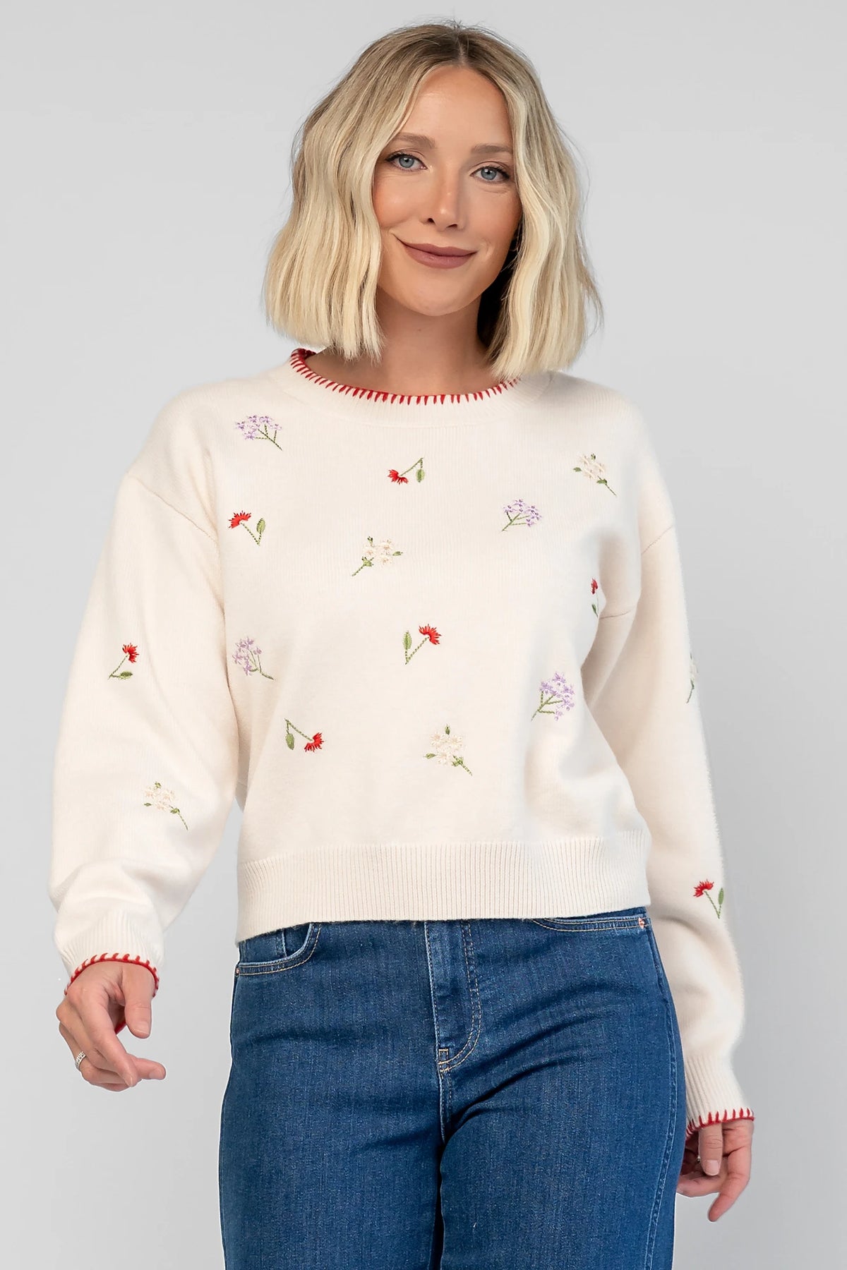 Ottilie Sweater in Cream with embroidered floral details, round neckline, red knit piping, and long sleeves.